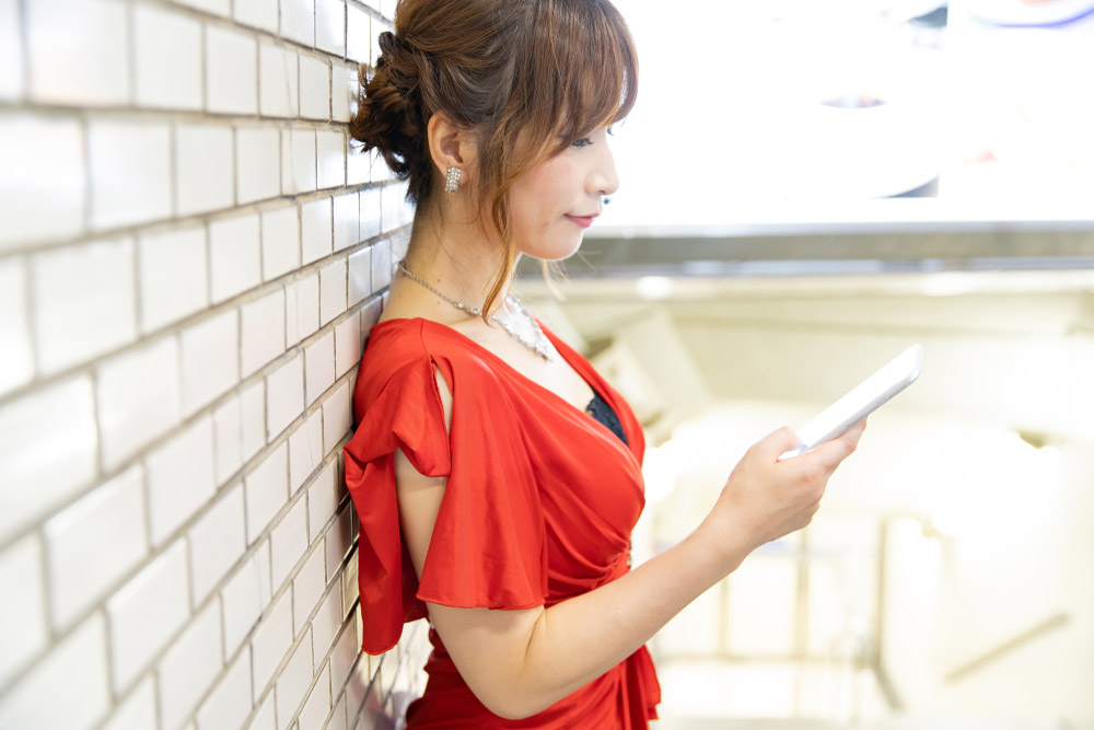 壁にもたれてスマホを扱うキャバ嬢